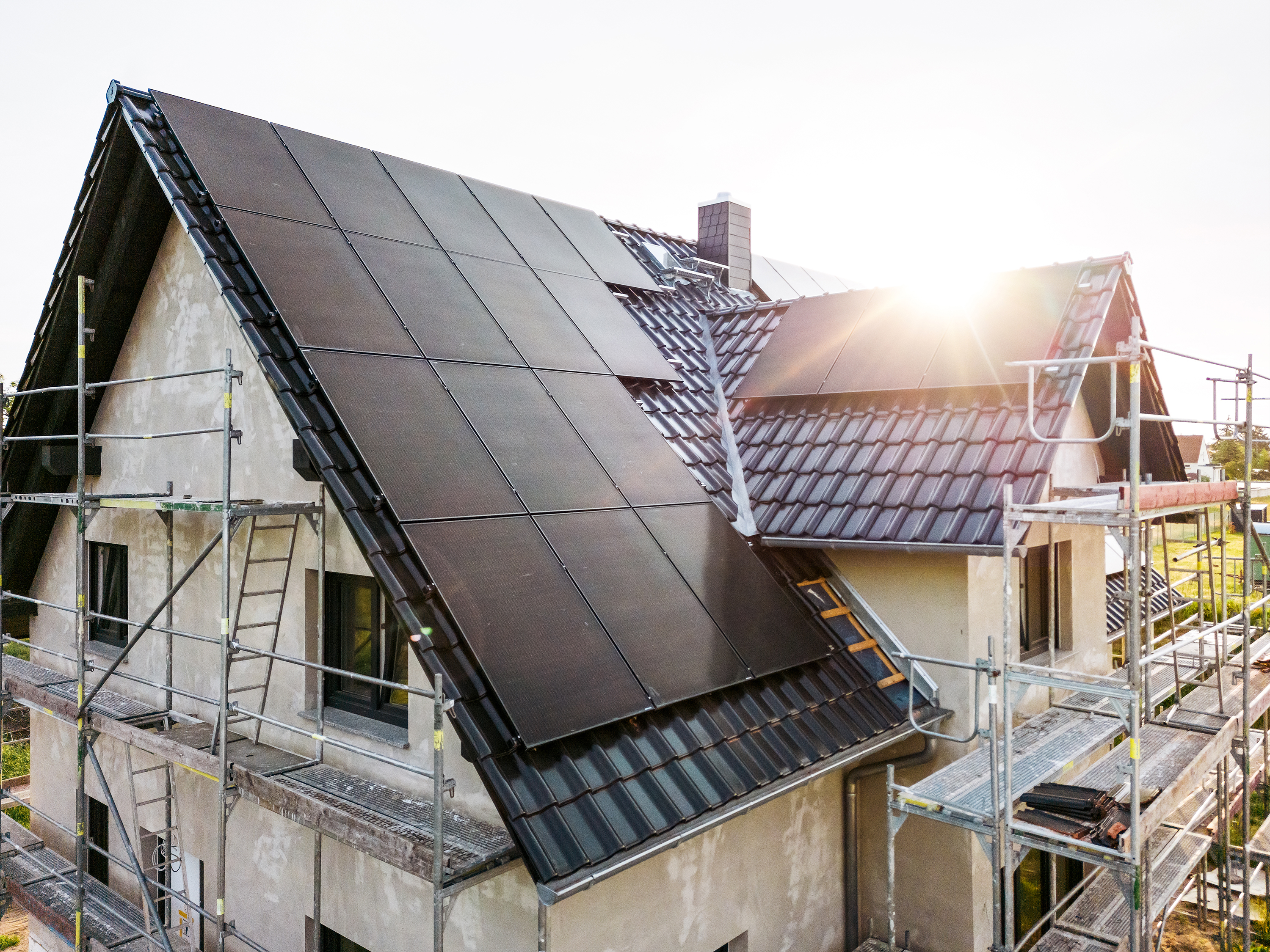 Ein Einfamilienhaus im Rohbauzustand mit Baugerüst und schwarzen Solarmodulen auf dem Dach bei Sonnenschein